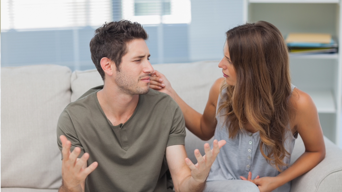 Man who looks concerned is speaking to his girlfriend while sitting on a white sofa