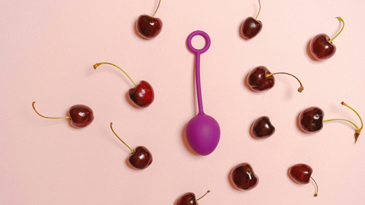 A purple Vibrating Love Egg placed on a vibrating light pink background surrounded by cherries