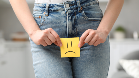 Girl with UTI in blue jeans holding a post it note with sad face below stomach 