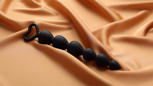 Black beginners anal beads with a love heart handle placed on gold silk sheets