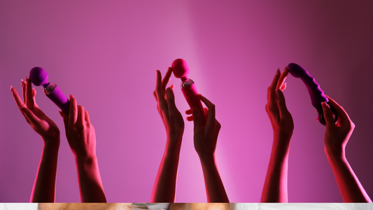 The hands of three woman each holding a vibrator in front of neon pink backrgound