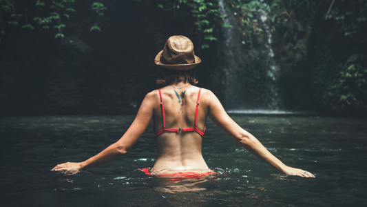 A with back to camera walking under a waterfall with arms out